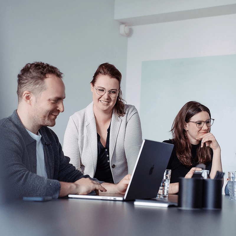 Drei Personen im Meeting arbeiten gemeinsam an einem Laptop