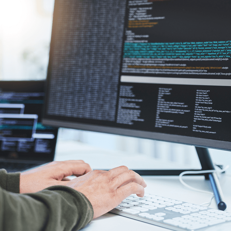 Hände eines Entwicklers tippen Code auf Tastatur vor großem Monitor