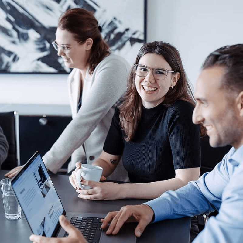 Drei mindtwo Teammitglieder im Meeting, lachend und konzentriert vor einem Laptop.